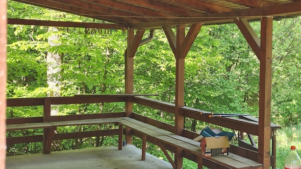 Un padiglione in legno all'aperto con panche e tavolo, immerso nel verde.