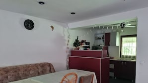 Un'area pranzo con tavolo e sedie, una cucina sullo sfondo e una ventola a soffitto.