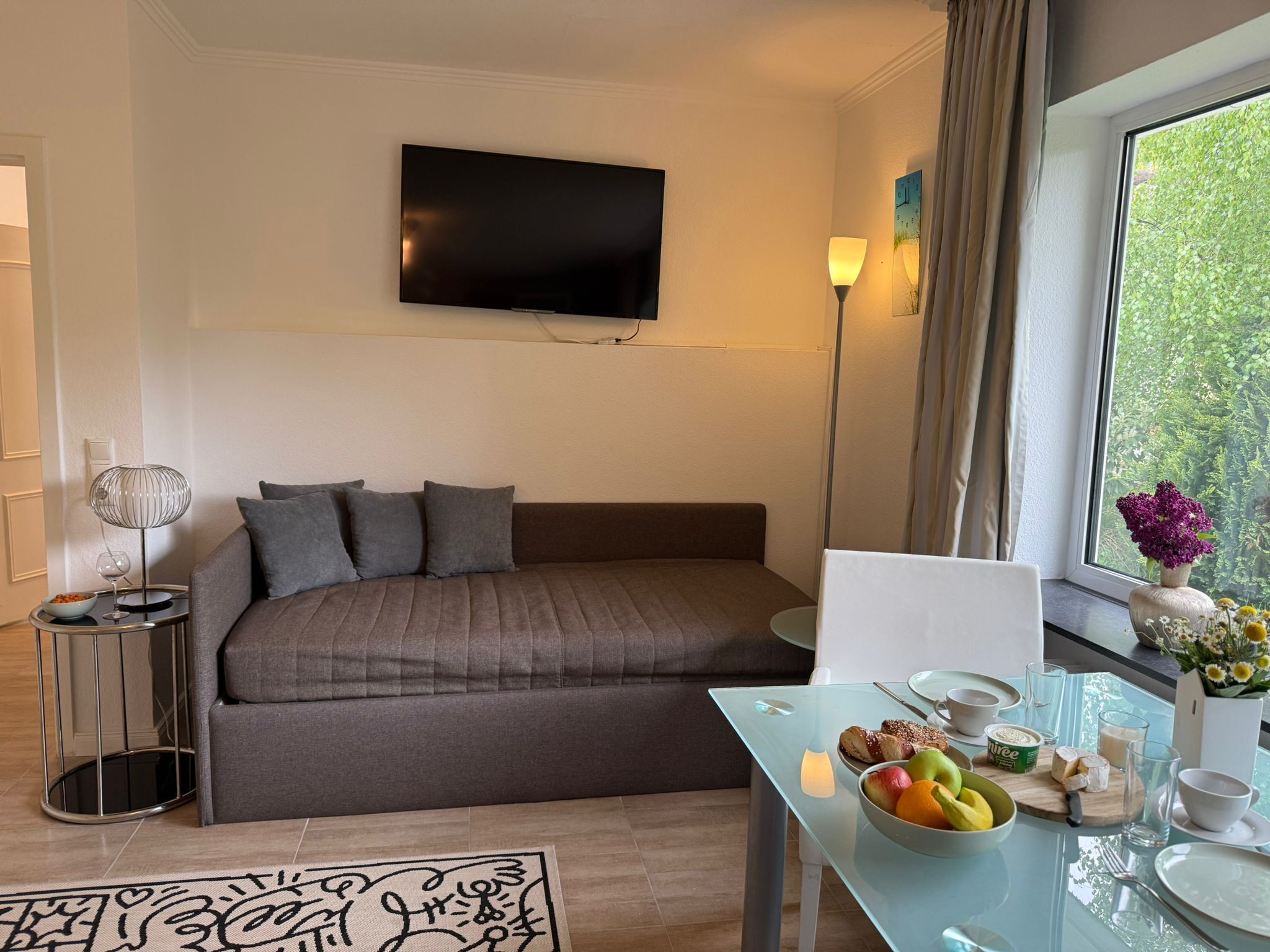 Ein modernes Hotelzimmer mit Bett, Flachbildfernseher, Esstisch mit Frühstück und großem Fenster.