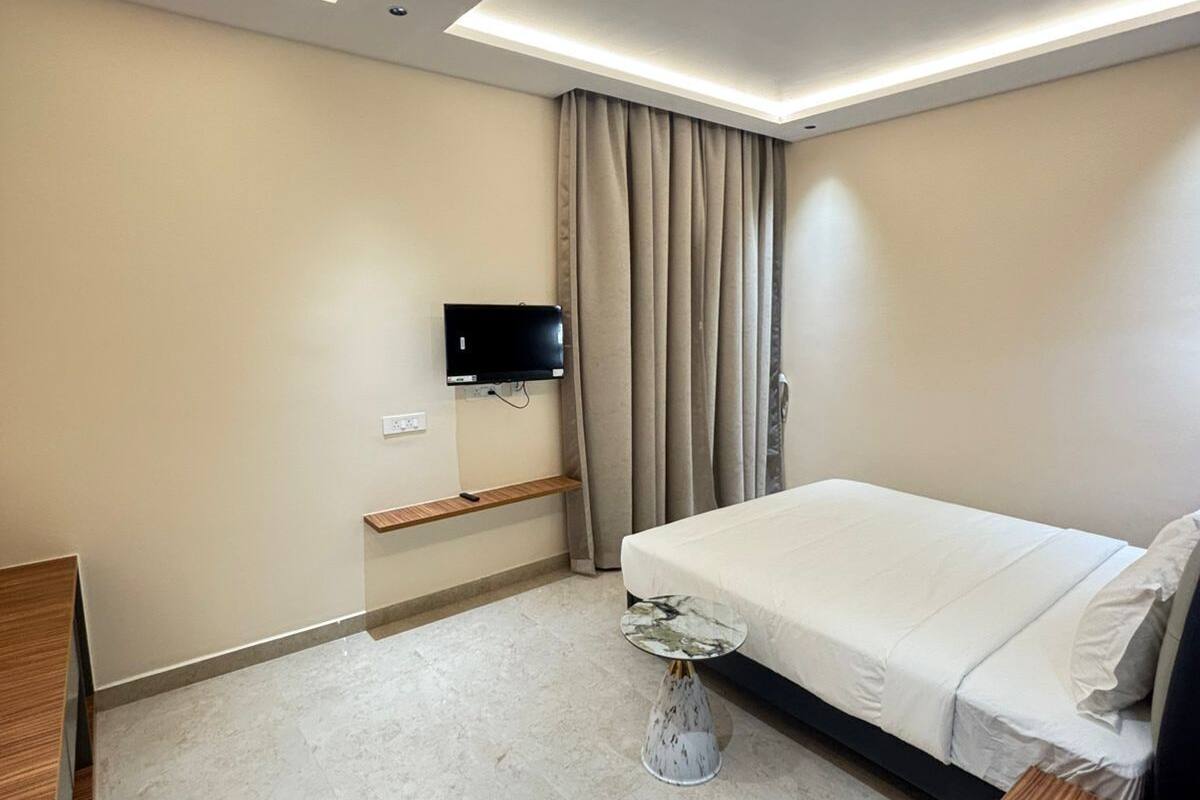 Ein modernes Hotelzimmer mit Bett, Wand-Fernseher, einem kleinen Beistelltisch und einem Nachttisch aus Holz.