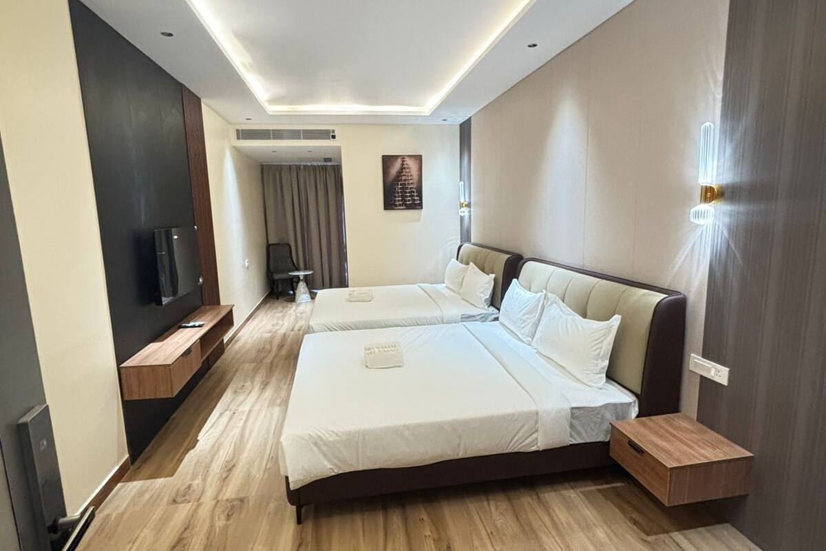 Ein modernes Hotelzimmer mit zwei Betten, Holzboden, einem Flachbildfernseher, einer Wandleuchte und einem kleinen Tisch.