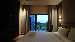 Ett hotellrum med en stor säng, en tv, en balkong med utsikt över omgivningarna och ett litet bord.