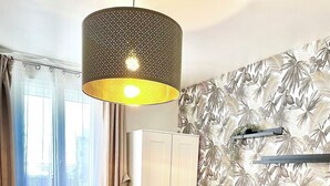 Ein Schlafzimmer mit einem Bett, einem Kleiderschrank, einem Heizkörper, einer Pendelleuchte und einem Fenster mit Vorhängen.