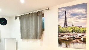 Ein Essbereich mit einem für zwei Personen gedecktem Tisch, einer Uhr und einem Fenster mit Vorhang.
