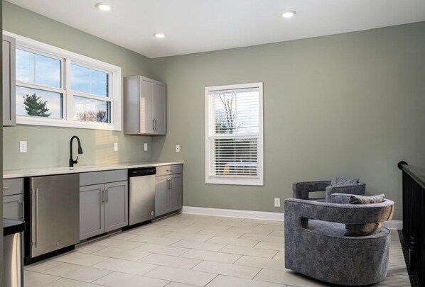 A modern kitchen with grey cabinets, stainless steel appliances, and a large window with blinds.