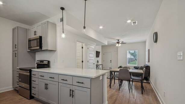 A modern kitchen with grey cabinets, stainless steel appliances, and pendant lighting.