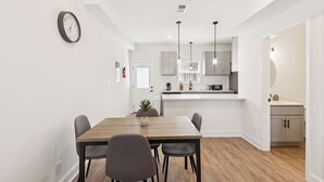 A modern kitchen with white cabinets, a wooden dining table, and pendant lights.