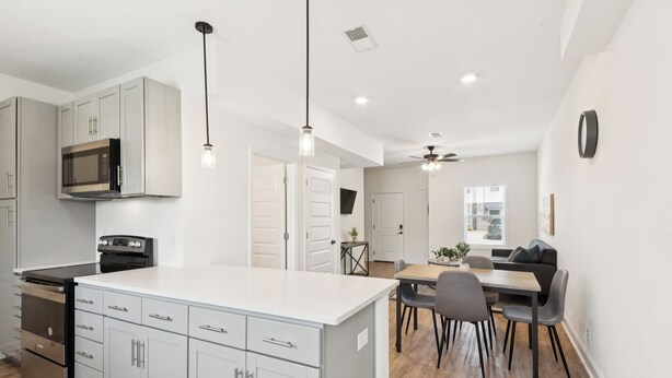 A modern kitchen with white cabinets, a microwave, and a stove. There is a dining area with a table and chairs.