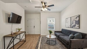 A living room with a flat-screen TV, a ceiling fan, a sofa, a coffee table, and a rug.