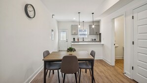 A modern kitchen with white cabinets, a wooden dining table, and pendant lights.