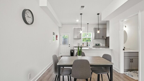 A modern kitchen with white cabinets, a wooden dining table, and a clock on the wall. - Arte Luxury townhomes O5 I Comfy 2 Bed 2.5 Bath (Clarksville)