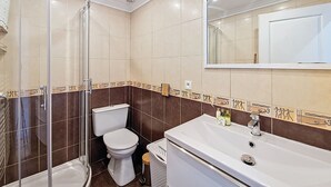 A bathroom with a glass shower enclosure, a toilet, a sink with a mirror above it, and decorative tiles along the baseboards. - N&J - CASA SOLANA - Terrace - Centre (Niza)