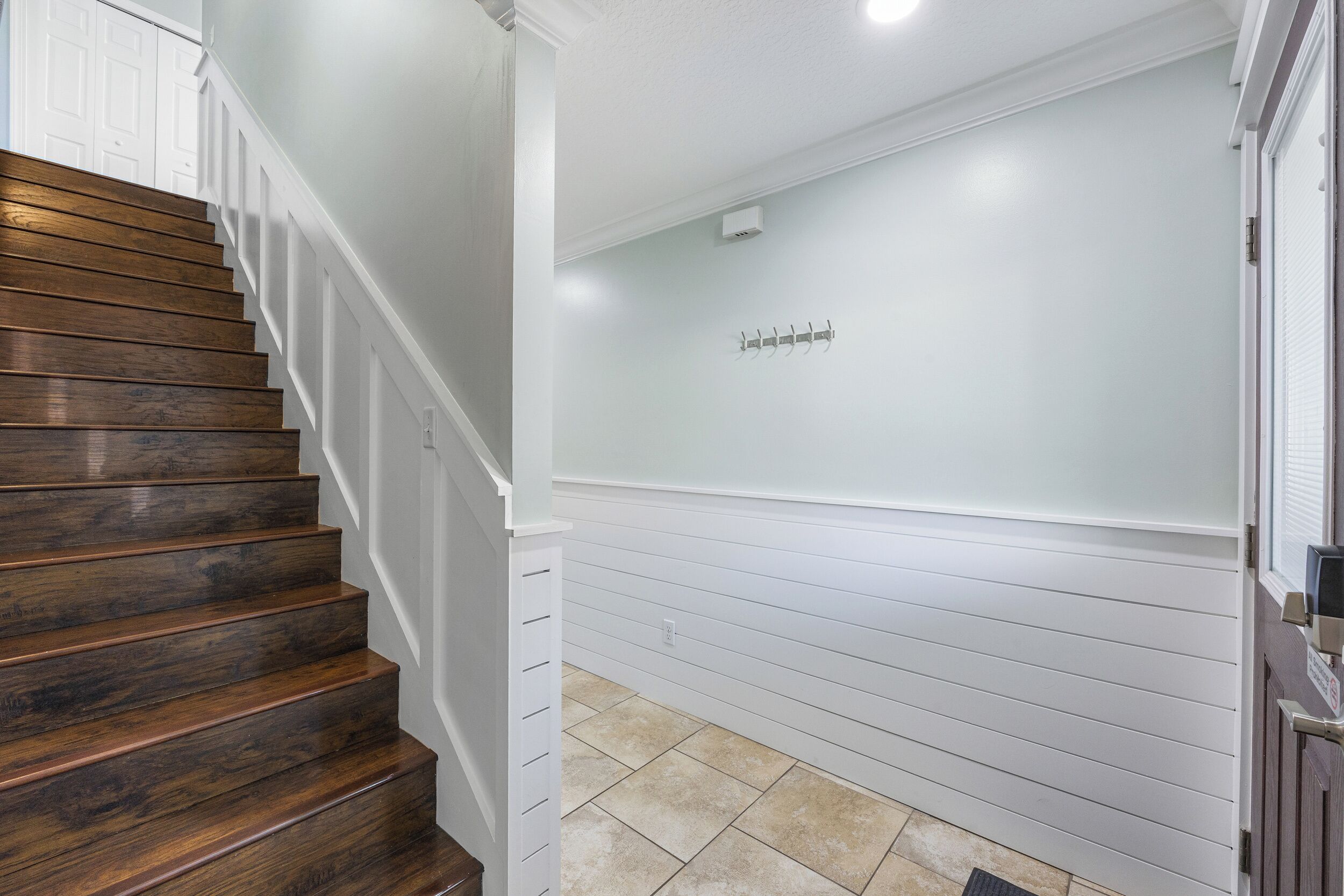 Una escalera con escalones de madera y barandillas blancas que lleva a un rellano con una pared de tono claro y una unidad de aire acondicionado pequeña montada en ella.