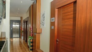 A hallway with wooden flooring, a wooden door labeled '203', and a wall-mounted sign with a floral design. - Hotel S K Executive (Rajgurunagar)
