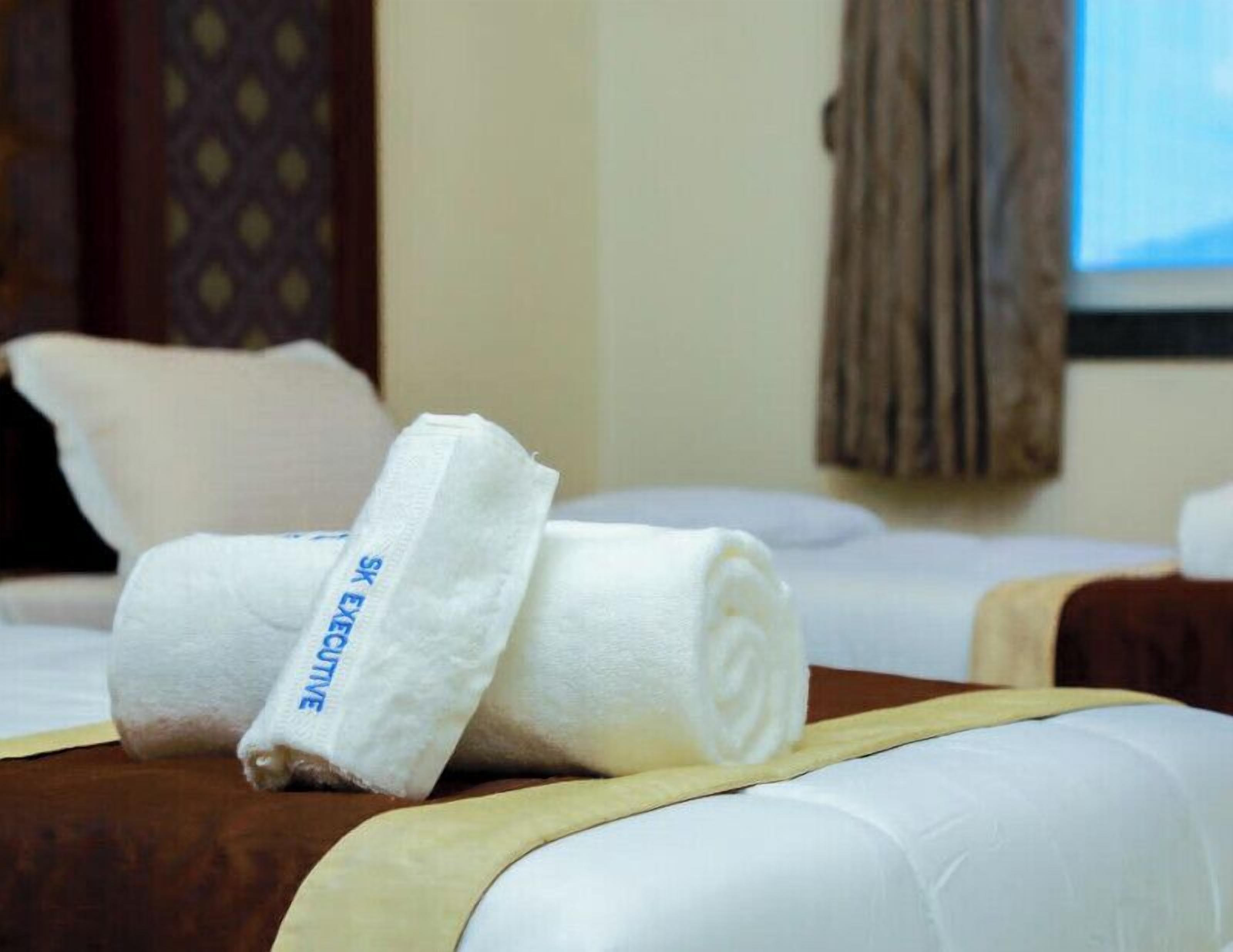 A hotel room with neatly made beds, a visible window with curtains, and a patterned wall design.