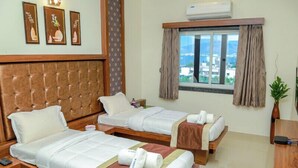 A hotel room with two beds, a large window with curtains, a wall-mounted air conditioner, and framed artwork on the wall. - Hotel S K Executive (Rajgurunagar)