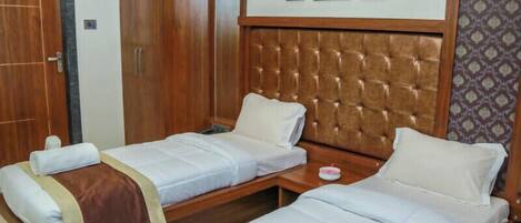 A hotel room with two single beds, a wooden wardrobe, and a tufted headboard.
