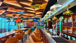 Una zona de bar con diversas opciones de asientos, una barra con un barista y una pantalla mostrando un evento deportivo.