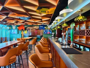 Una zona de bar con diversas opciones de asientos, una barra con un barista y una pantalla mostrando un evento deportivo.