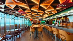 Una zona de bar moderna con una barra larga, varios taburetes y una pantalla de televisión.