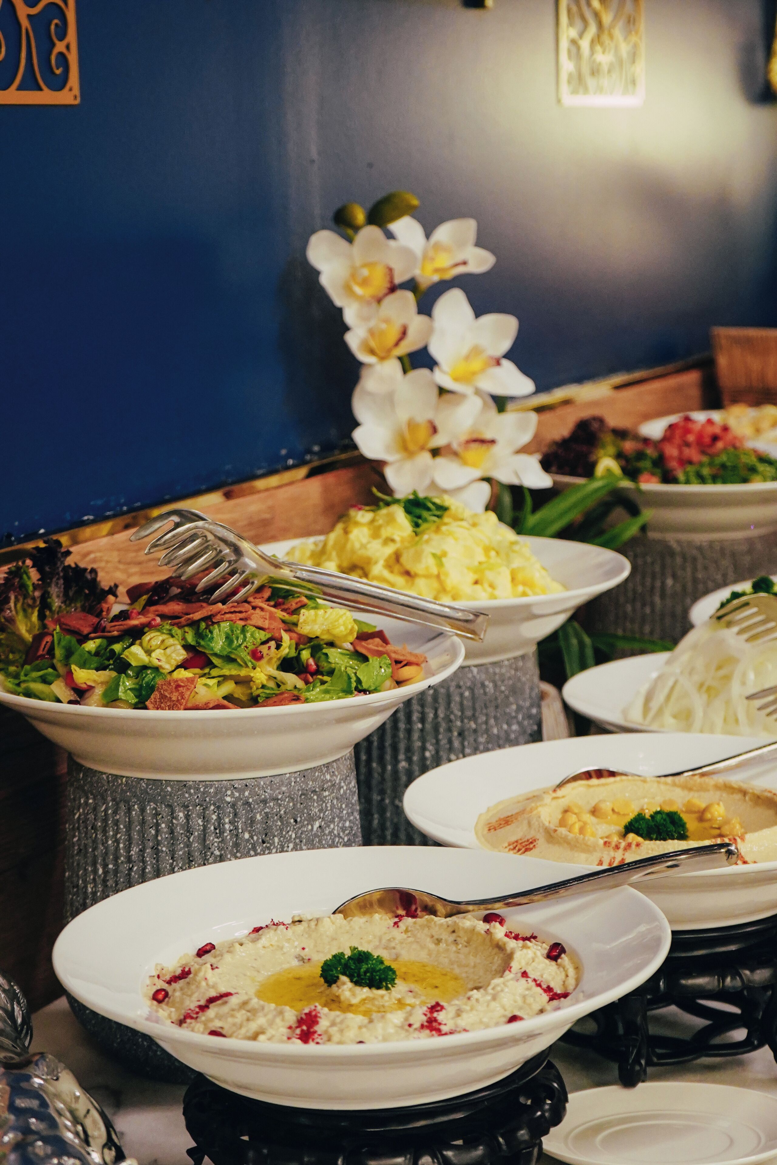 A variety of dishes on a buffet table with a decorative orchid arrangement in the background.