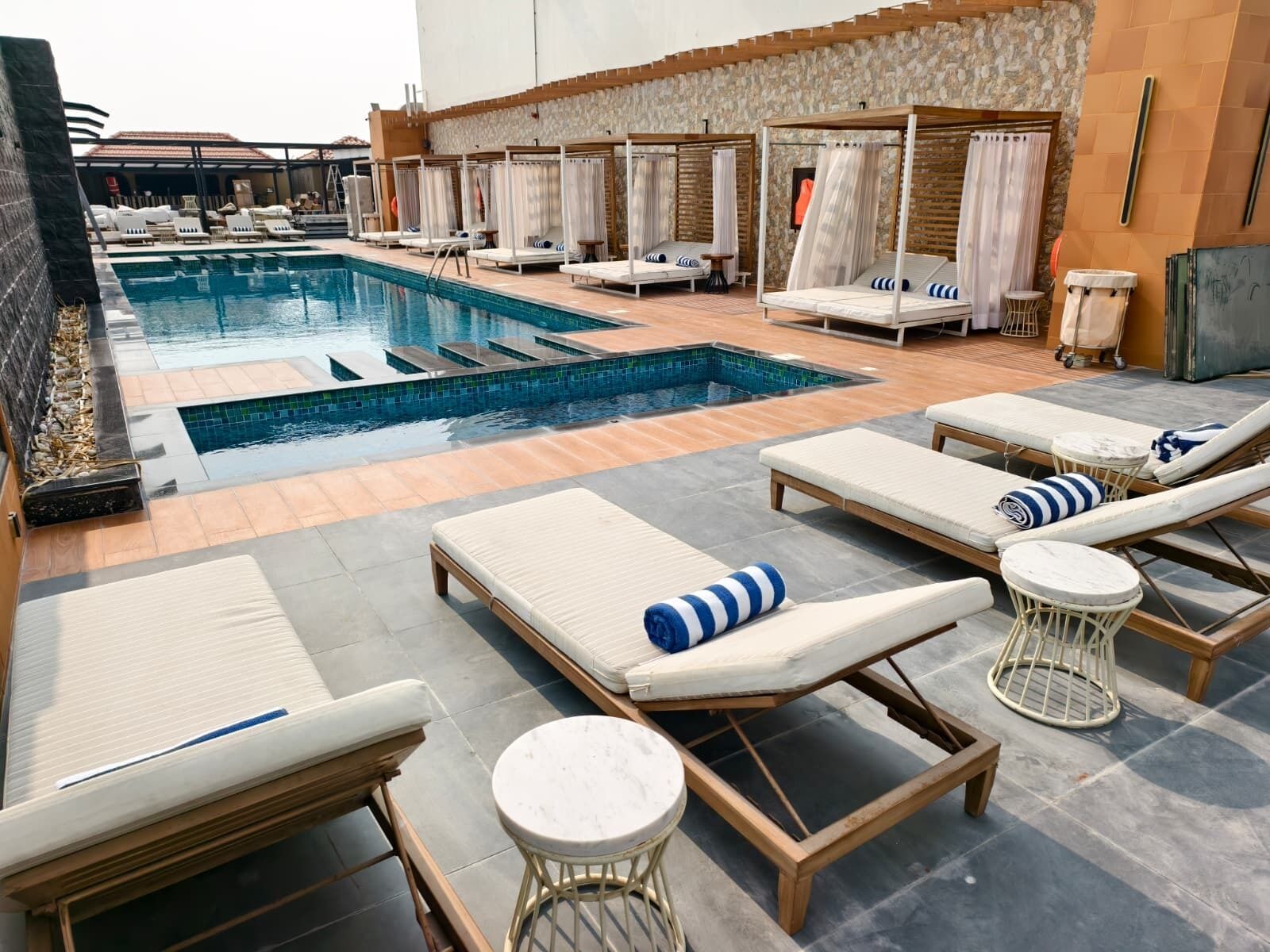 Zona junto a la piscina con sillones de descanso, una bañera de hidromasaje y un muro de piedra.