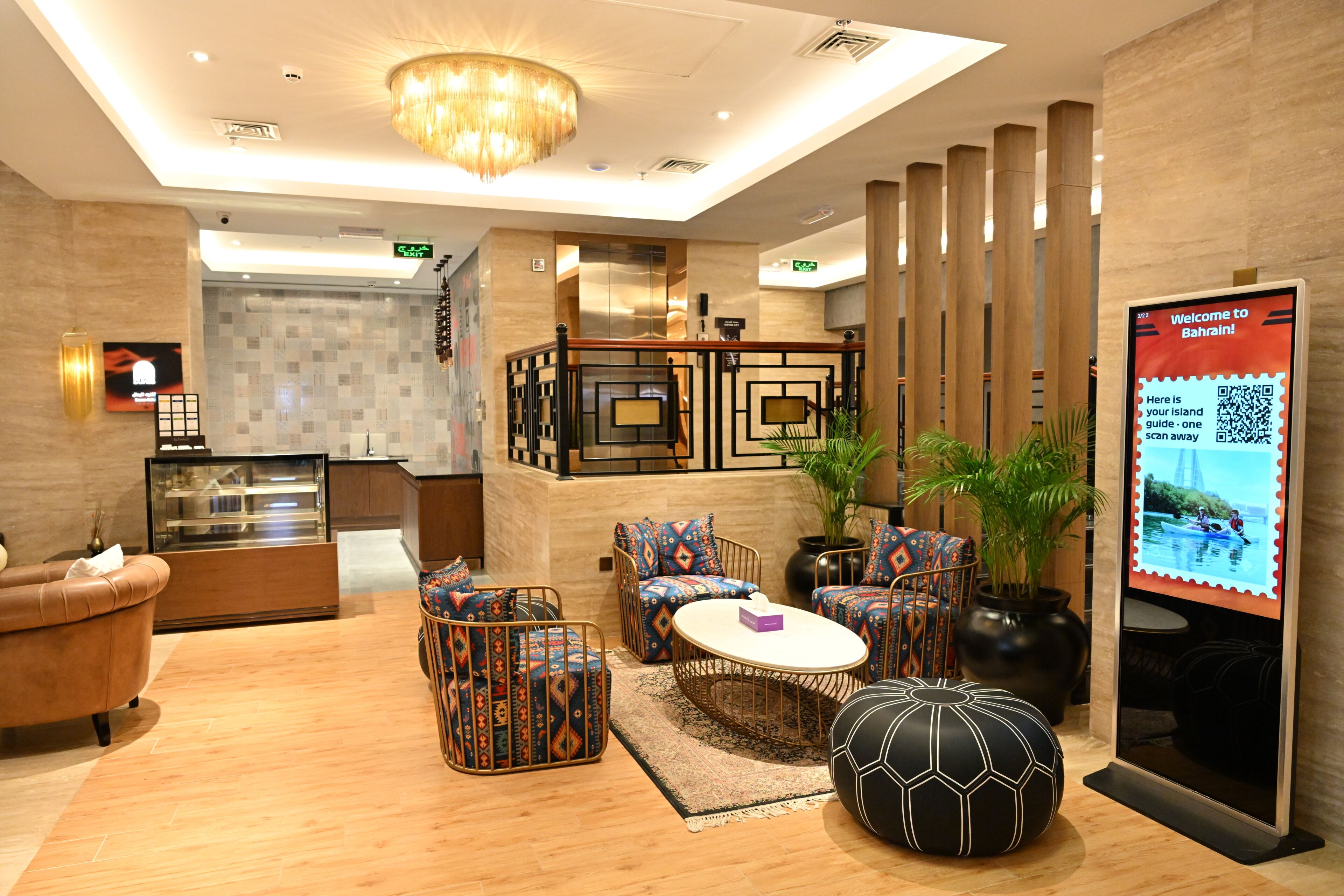 A hotel lobby with a reception desk, seating area with patterned sofas, a coffee table, a decorative black and white ball, and a welcome sign.