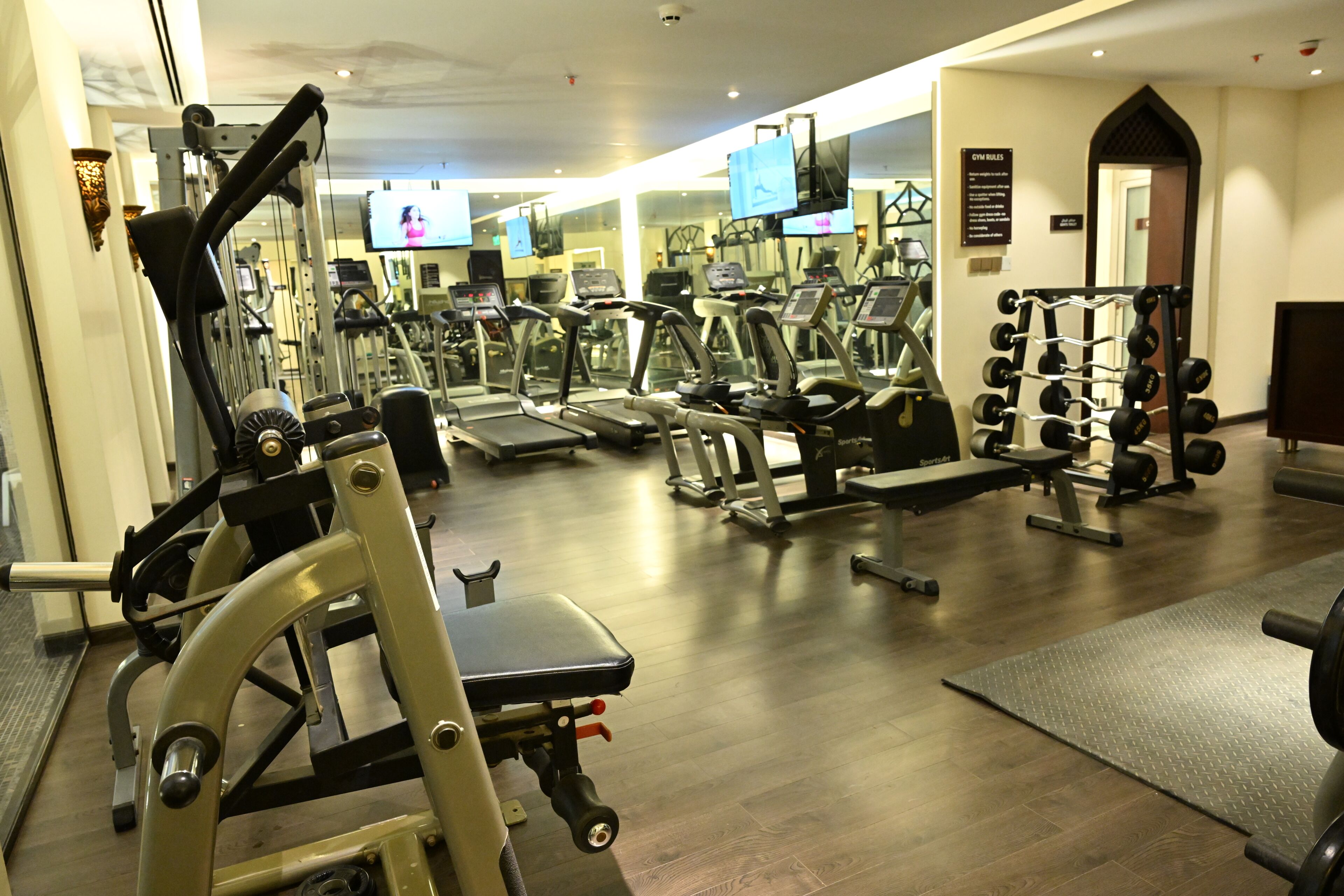 A gym with various exercise equipment, including treadmills, weight machines, and a rack of dumbbells.