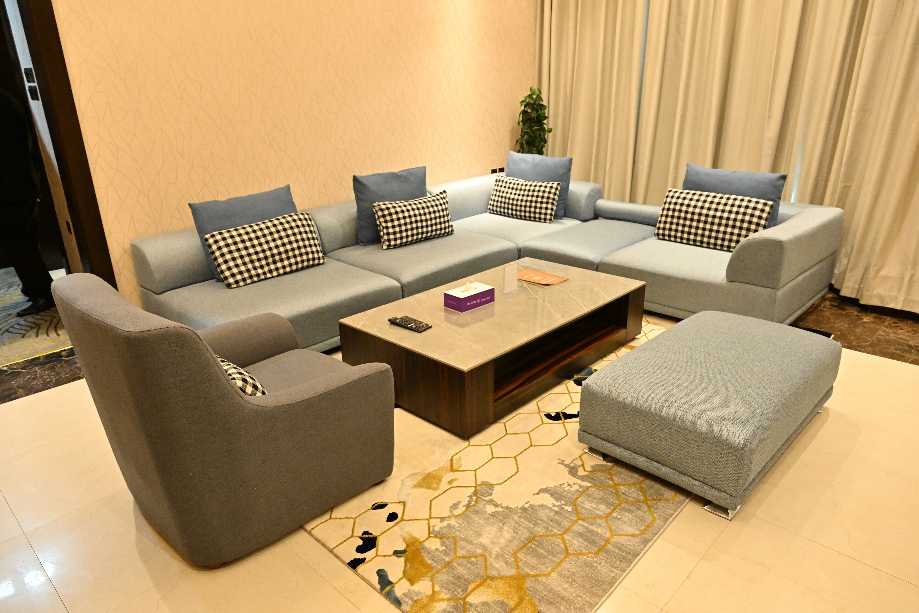 A modern living room with a grey sectional sofa, a matching ottoman, a coffee table, and a patterned rug.