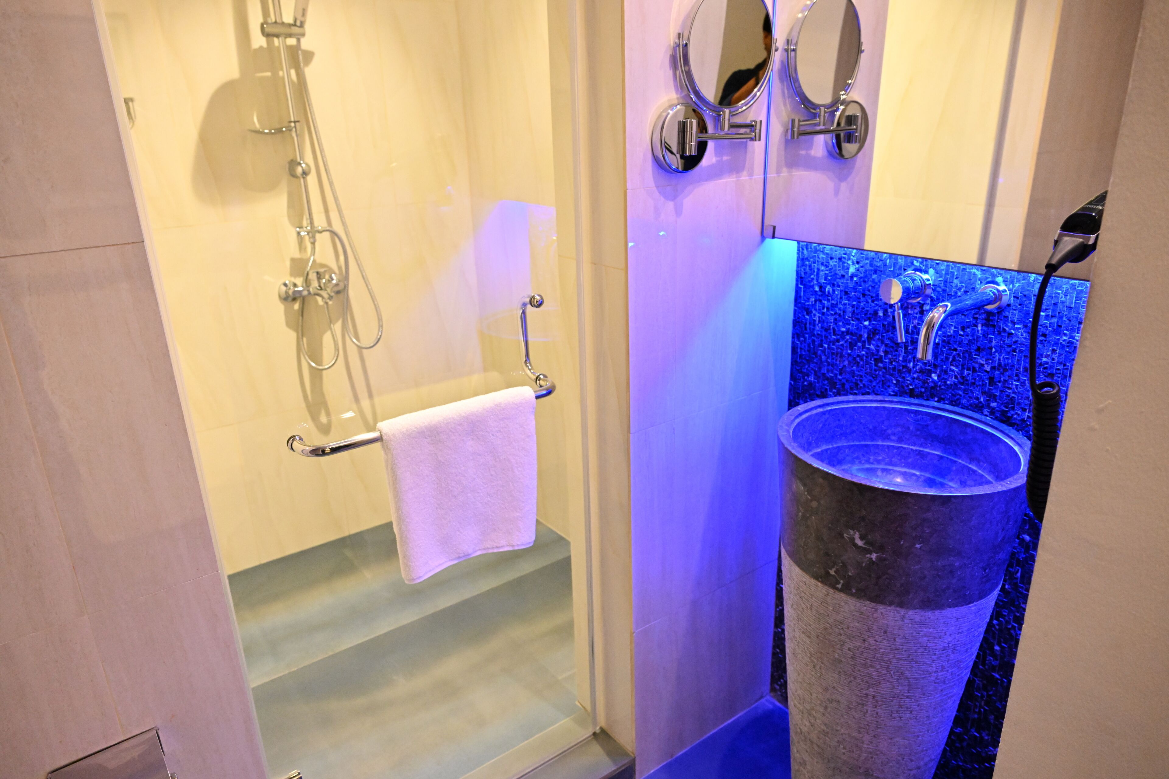 A bathroom with a glass-enclosed shower, a large sink with a blue mosaic backsplash, and a towel rack with a white towel.