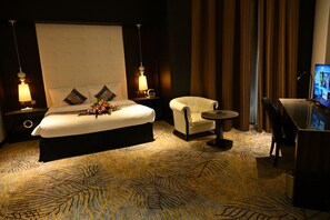 A hotel room with a large bed, two bedside lamps, a small round table, a chair, and a desk with a computer. - Savoy Grande Hotel and Spa (Manama)