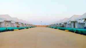 A row of white tents with green awnings, arranged in a symmetrical layout on a sandy ground. - Great Rann Resort (Bhuj)