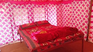 A bed with a red and black patterned bedspread, a wooden frame, and a pink and white floral curtain backdrop. - Great Rann Resort (Bhuj)