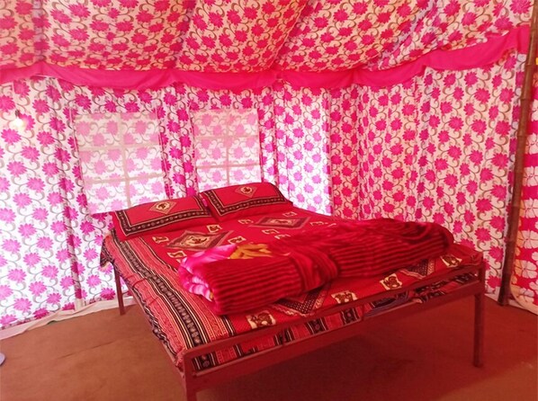 A bed with a red and black patterned bedspread, a wooden frame, and a pink and white floral curtain backdrop.