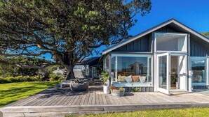 Een modern huis met een houten terras, grote ramen en een boom op de achtergrond.