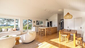 Een ruime woonkamer met een groot raam dat uitkijkt op een prachtig landschap, een houten eettafel en een gezellige zithoek met een grote loungestoel.