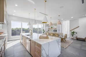 A modern kitchen with a marble island, pendant lights, and a dining area with a view.