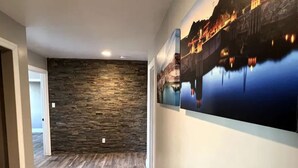 A hallway with a stone wall, wooden flooring, and a large cityscape painting on the wall.