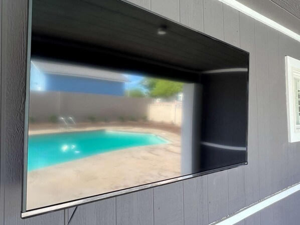 A wall-mounted TV displaying a backyard with a swimming pool.