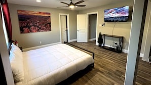 A bedroom with a bed, a ceiling fan, a mounted TV, and a painting on the wall.