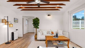 A modern living room with a wooden ceiling, a white sofa, a coffee table, and a large window.