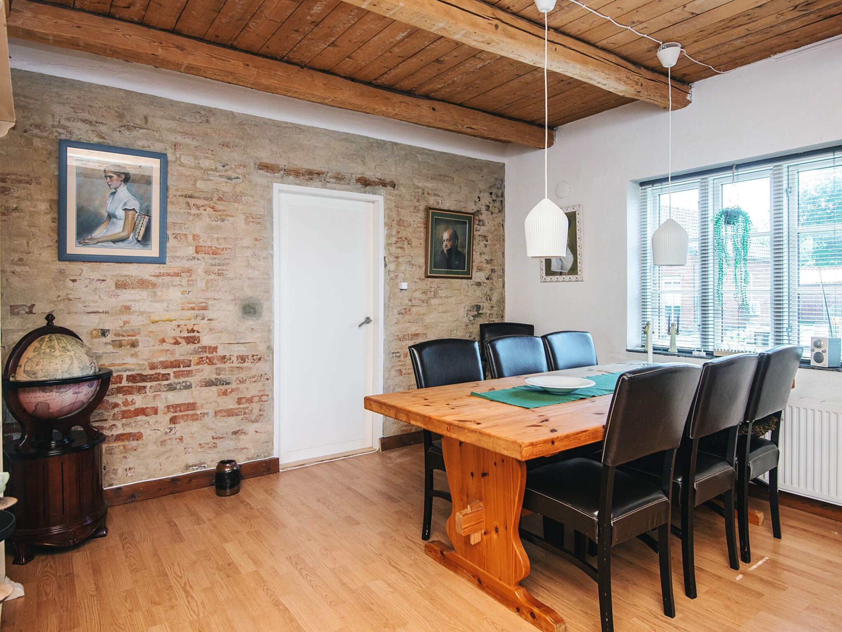 A dining area with a wooden table, black chairs, and a brick wall.