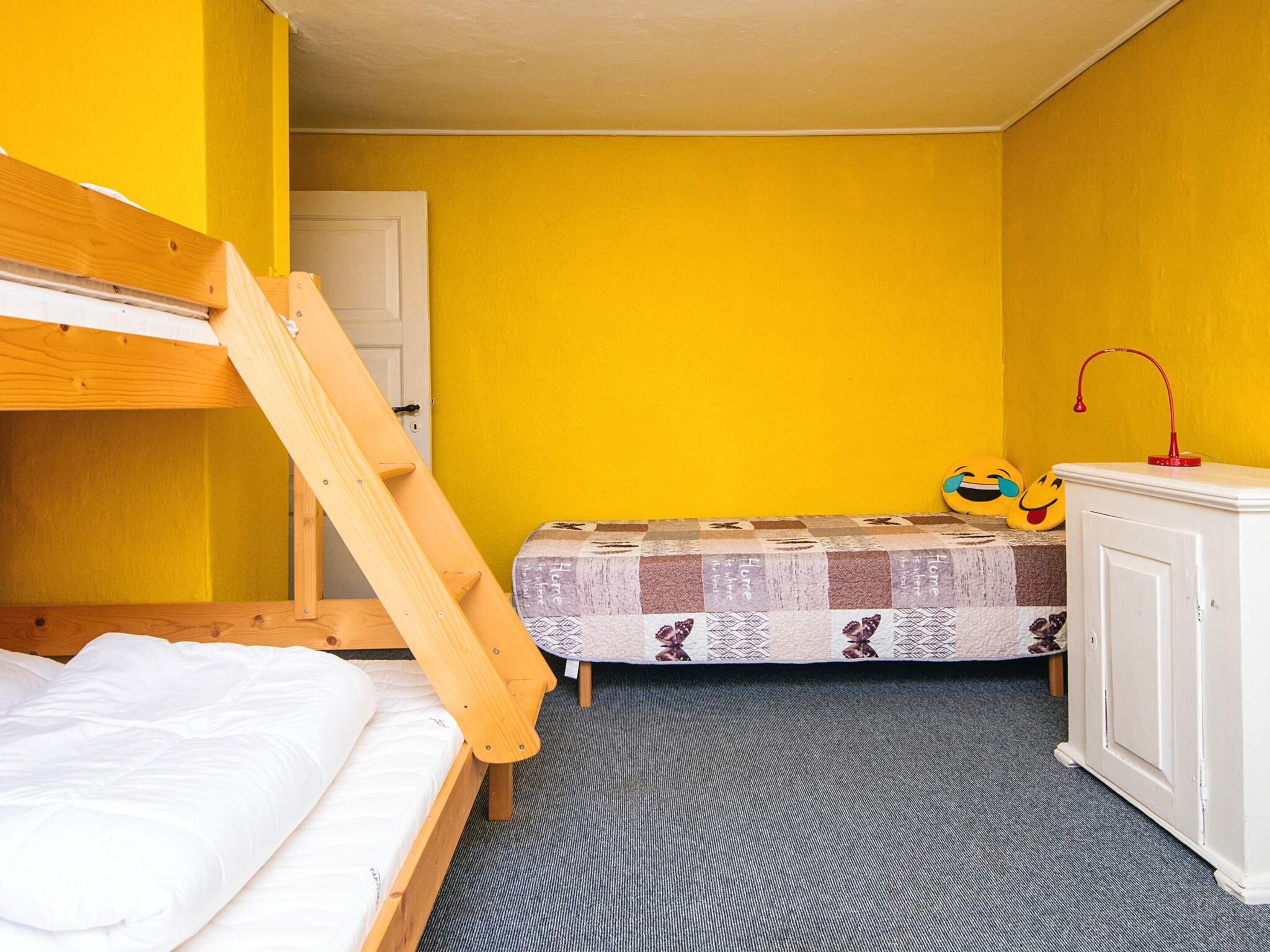 Pieni huone, jossa on kerrossänky, yksi erillinen sänky, työpöytä tuolilla ja ovi.