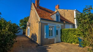 Une maison à deux étages, avec un toit recouvert de tuiles rouges, une cheminée et un petit garage attenant.