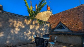Une terrasse avec une table et des chaises, un mur recouvert de plantes grimpantes et un bâtiment doté d’un toit en tuiles et d’une cheminée.