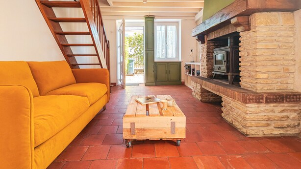 Un salon chaleureux avec un escalier en bois, un canapé jaune, une cheminée en pierre et une table basse en bois.
