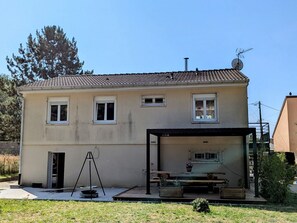 Kaksikerroksinen talo, jossa on katettu terassi, satelliittiantenni ja pieni puutarha.