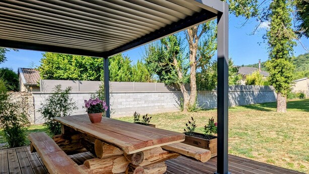 Eine Holzterrasse mit Picknicktisch und Bänken, umgeben von einem Garten und einem weißen Zaun.