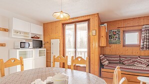 Een gezellige kamer met houten inrichting, een eettafel met stoelen, een magnetron, een koelkast en een bank met decoratieve kussens.