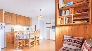 Een gezellige woonkamer met een bank en een klein tafeltje, houten boekenkasten, en een keuken met houten kasten en een eettafel.